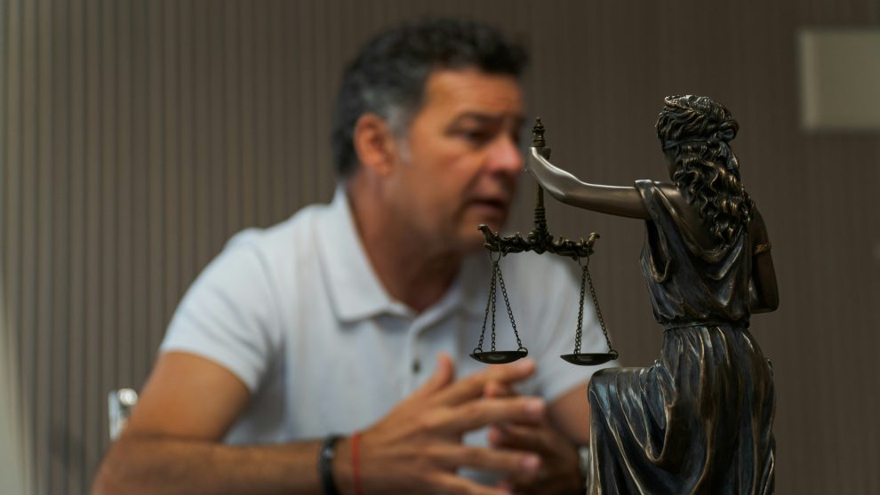man sitting at a table with lady justice statue in front of him