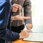 two people, one signing documents and the other handing over keys