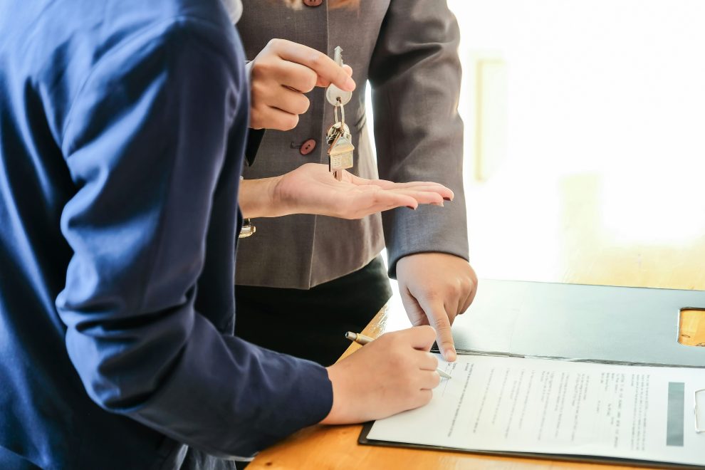 two people, one signing documents and the other handing over keys
